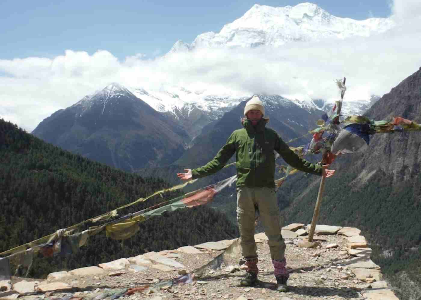 a lone hiker stands with prayer flags with the annapurna range in the background