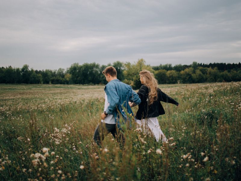 young travel companions walking through long green grass in a meadow