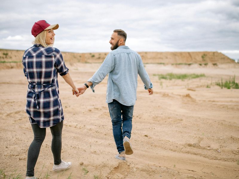 a young couple walk hand in hand on a sandy beach 